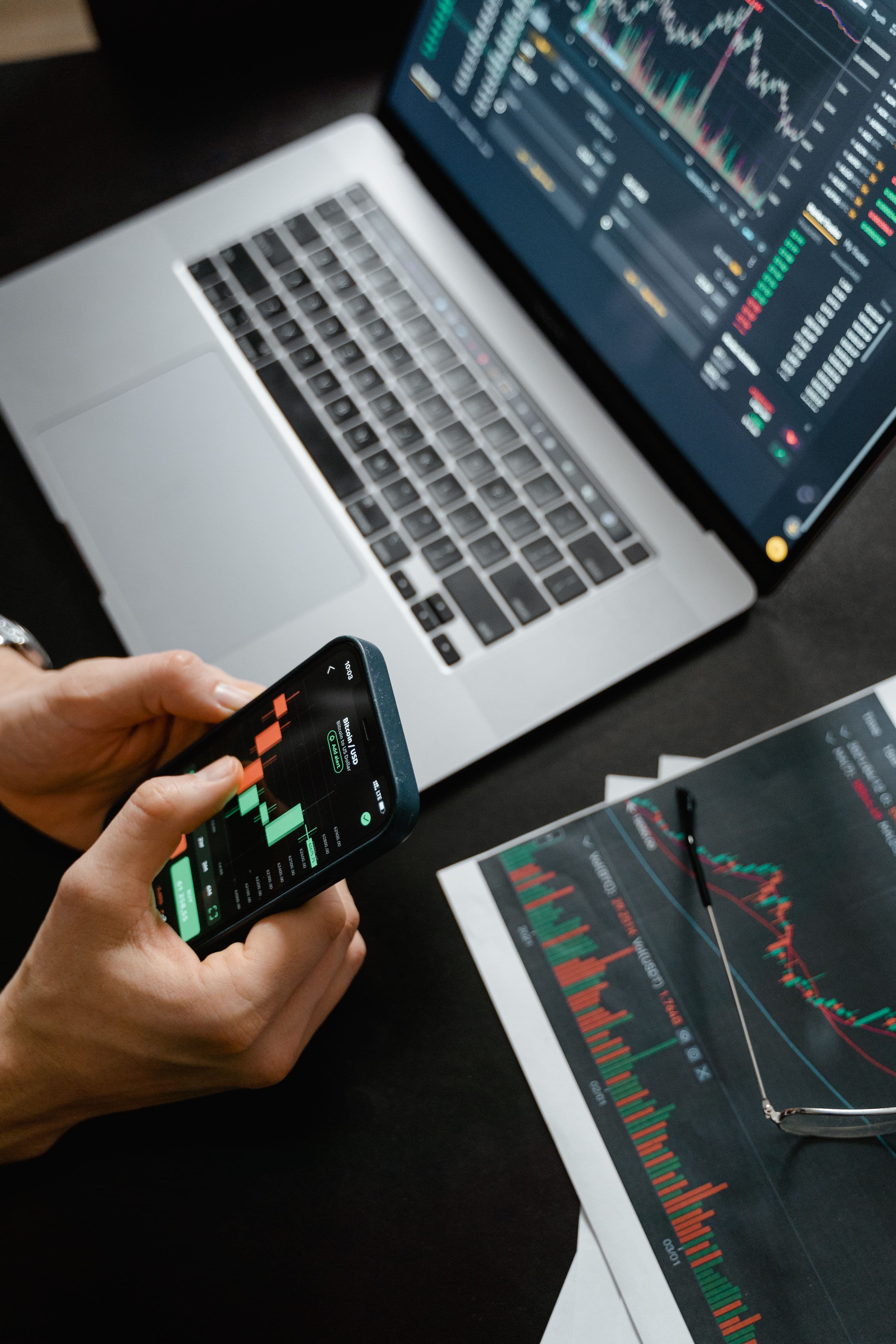 Financial charts on phone, laptop, and desk